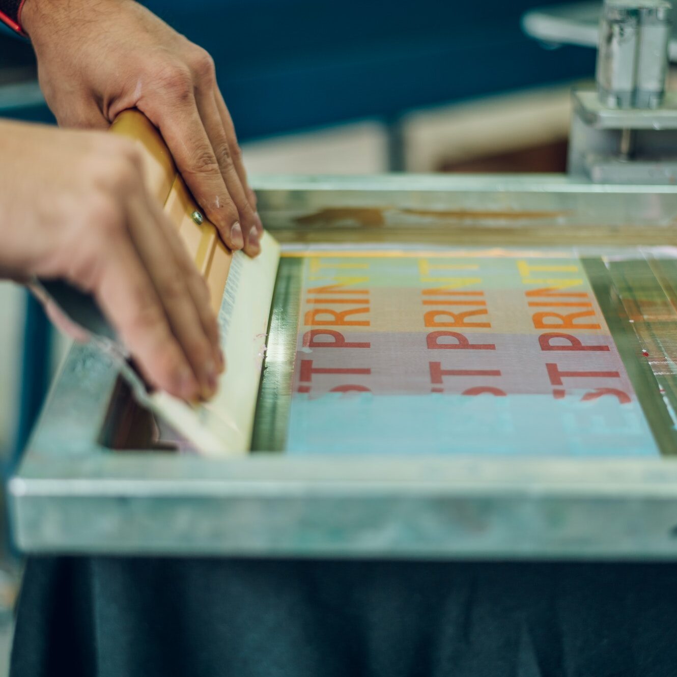 Male worker pressing ink on frame while using the printing machine in a workshop